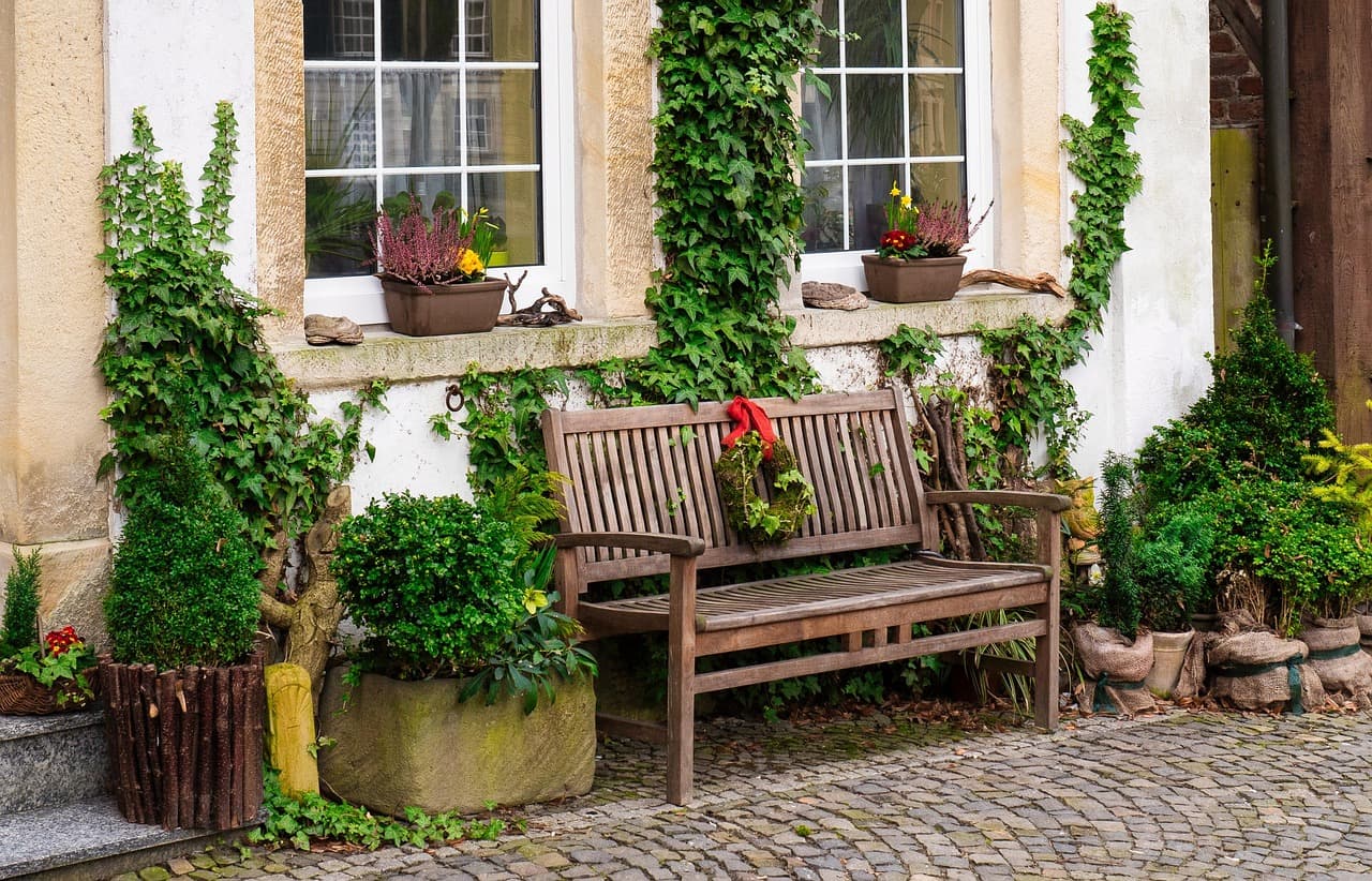Cobblestone front walk with a bench, containers, and vines climbing a house facade.